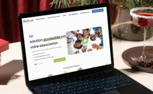 Un ordinateur portable posé sur une table affiche un site Web intitulé « La solution accessible pour votre association ». Larrière-plan présente des décorations festives, notamment une branche de pin verte, un cocktail rouge et un petit cadeau.